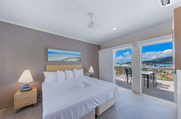 Modern hotel room with sea view balcony, spacious bed, elegant decor, and natural light perfect for relaxation.