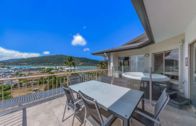 Scenic hotel balcony with stunning ocean and marina view, outdoor dining, and private hot tub under clear blue skies.