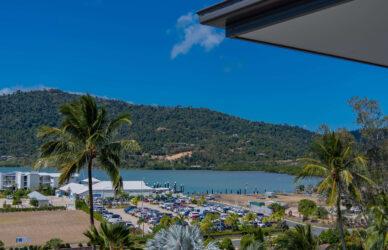Scenic view of marina with palm trees and lush mountains from hotel balcony, perfect for relaxation and nature lovers.