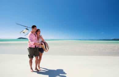 Couple on Whitehaven Beach in the Whitsundays with helicopter in background