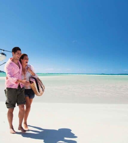 Couple on Whitehaven Beach in the Whitsundays with helicopter in background