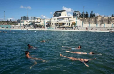 Guests enjoying a relaxing swim in a sunlit, modern hotel pool with nearby beachfront views and contemporary amenities.