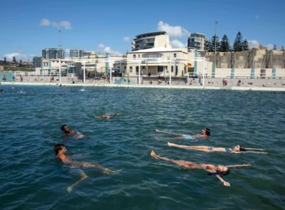 Guests enjoying a relaxing swim in a sunlit, modern hotel pool with nearby beachfront views and contemporary amenities.