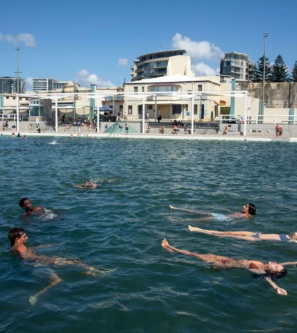 Guests enjoying a relaxing swim in a sunlit, modern hotel pool with nearby beachfront views and contemporary amenities.