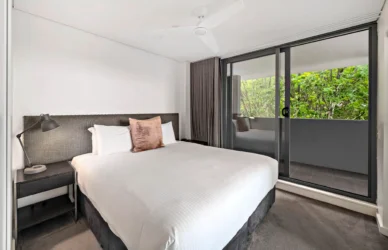 Spacious hotel room with king-size bed, modern decor, sliding balcony doors, and lush green view.