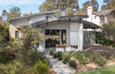 Modern boutique hotel villa with curved porte-cochère, sliding glass doors, potted flowers and landscaped garden path VIEW: front entrance